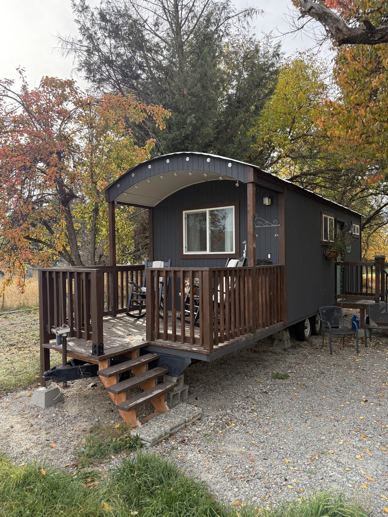 The dark gray Shepherd’s Hut with a wooden porch, surrounded by fall trees