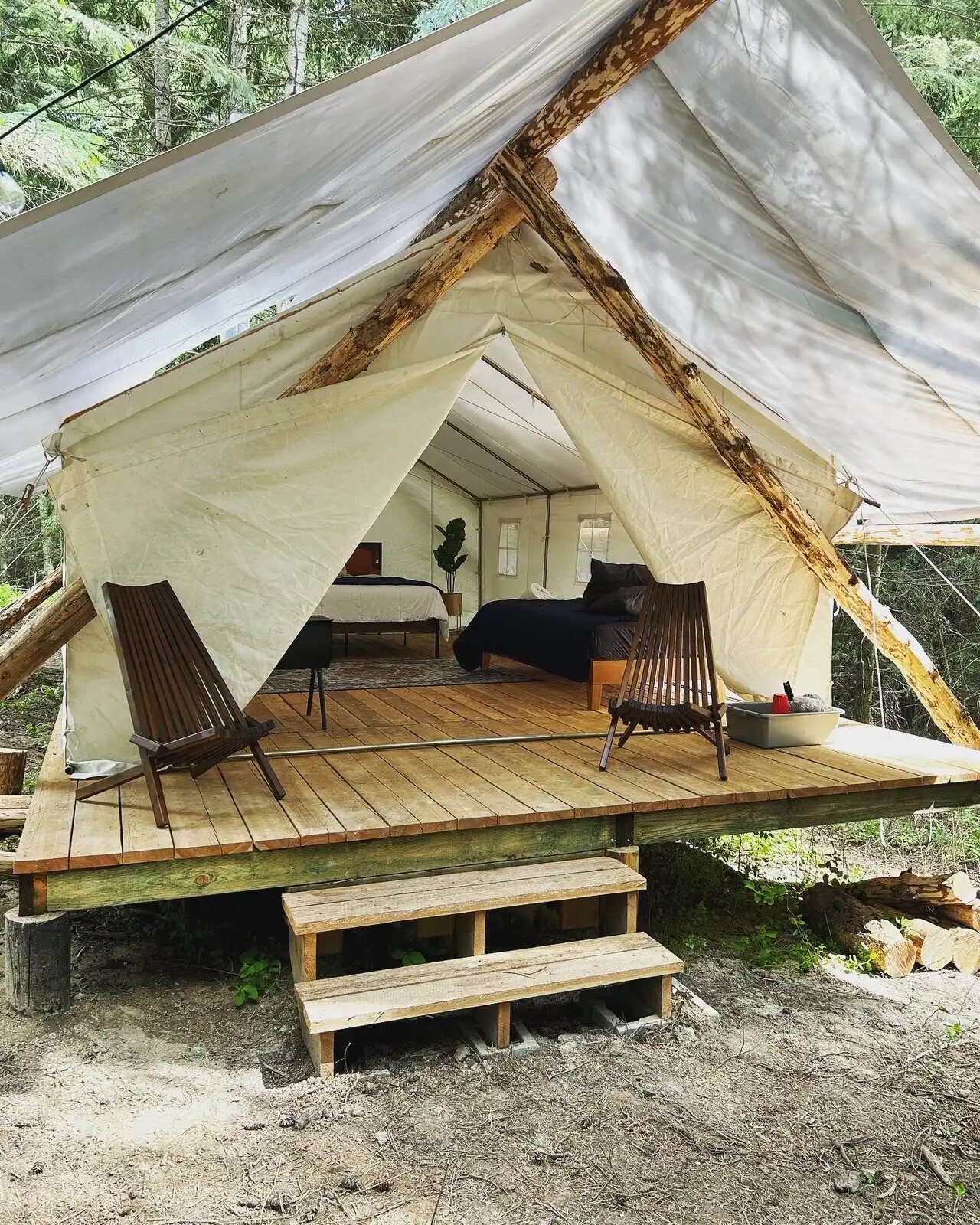 A canvas glamping tent on a wooden deck in the woods with two lounge chairs