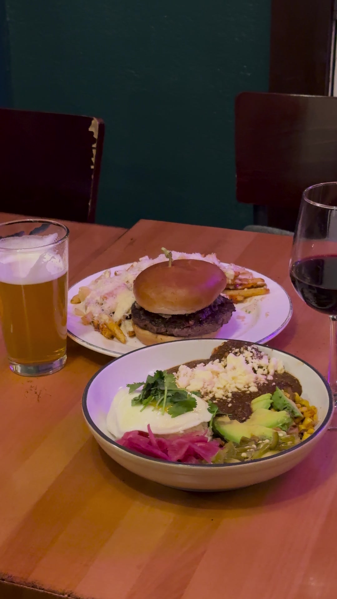 A burger, a colorful bowl, a beer and a glass of red wine on the table