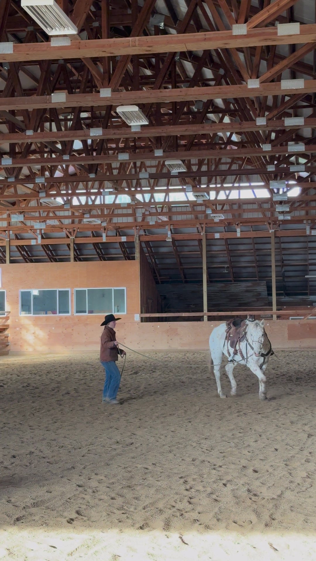 A wrangler working a horse in the indoor arena