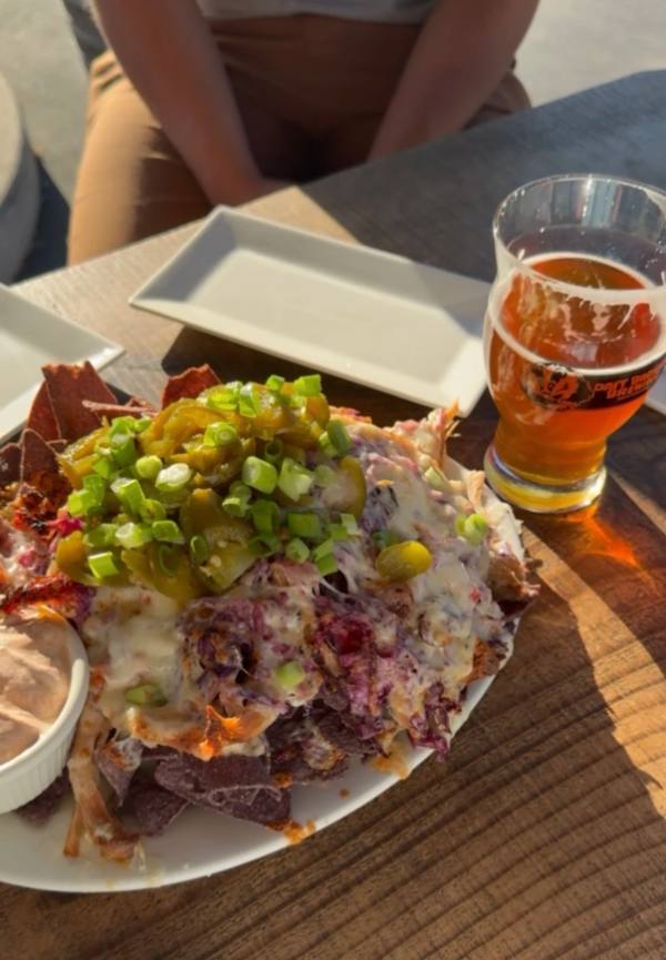 A loaded plate of food and a pint of beer on a sunny table